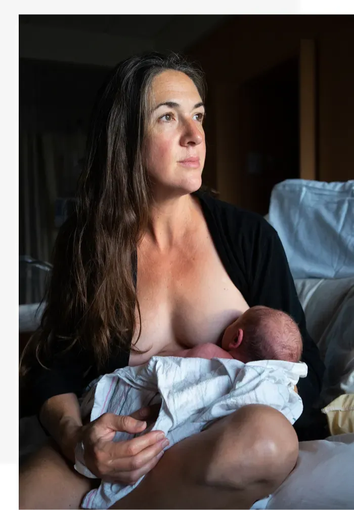 A mother breastfeeding her newborn beside a window